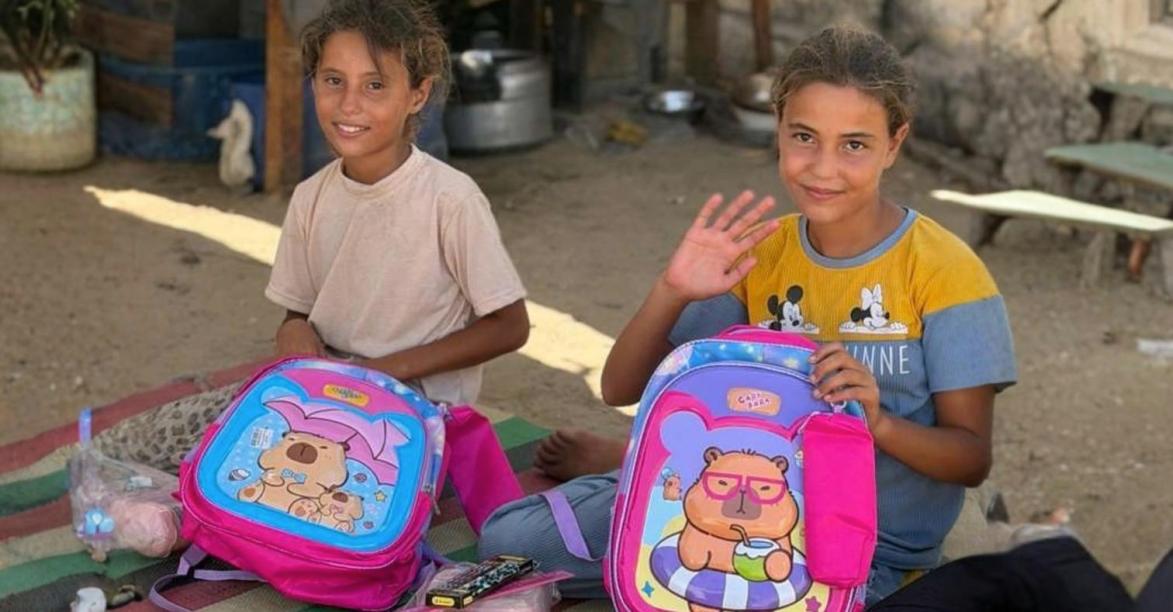 Two girls in Gaza smiling with their new school backpacks and supplies
